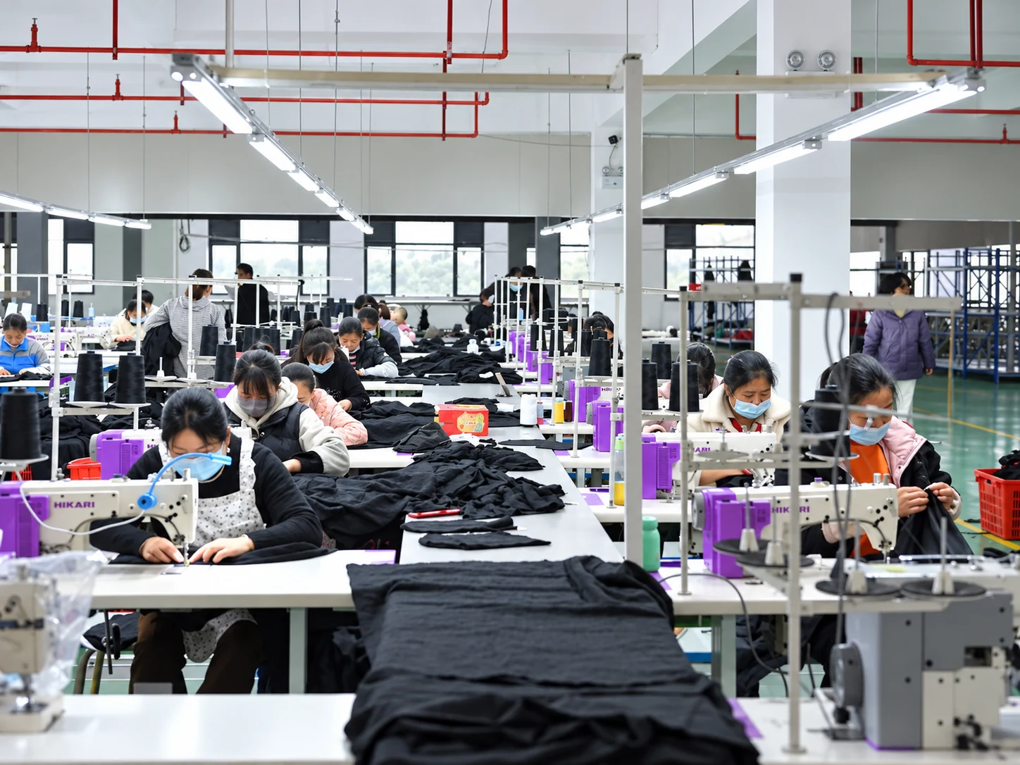 Teams assembling black garments across rows of sewing machines.