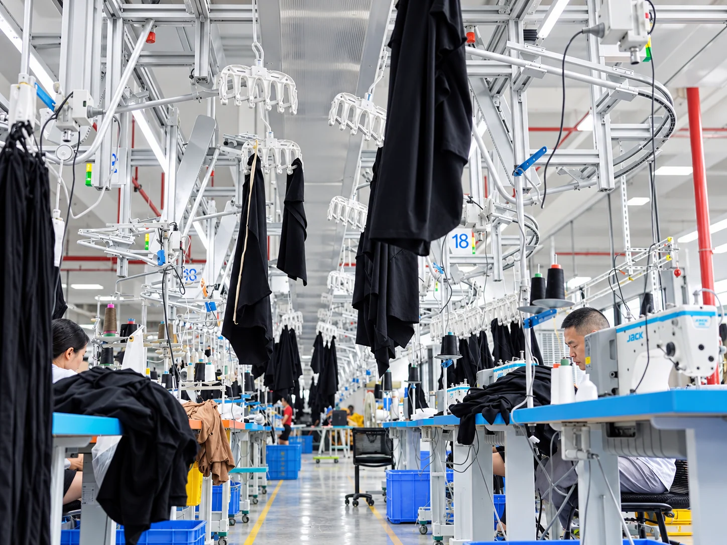 Garments moving between sewing stations on an overhead hanger system.